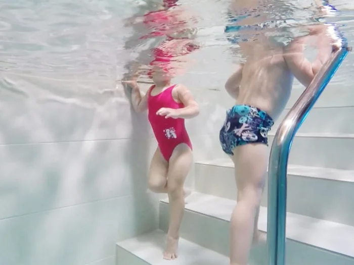Due bambini sulla scaletta della piscina termale, visti sott'acqua