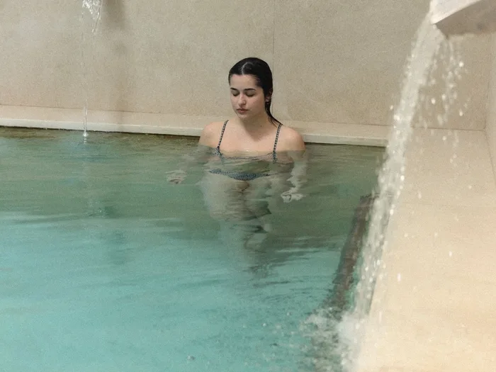 Una donna nella piscina termale, accanto alla cascata d'acqua