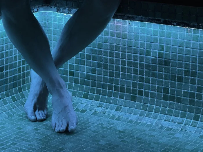 Gambe immerse nella piscina termale, con il mosaico azzurro sullo sfondo
